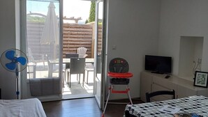A room with a bed, a table with a patterned tablecloth, a chair, a TV, and a sliding glass door leading to an outdoor patio with a table and chairs. - Le Clos de L'arc (Vallon Pont d'Arc)