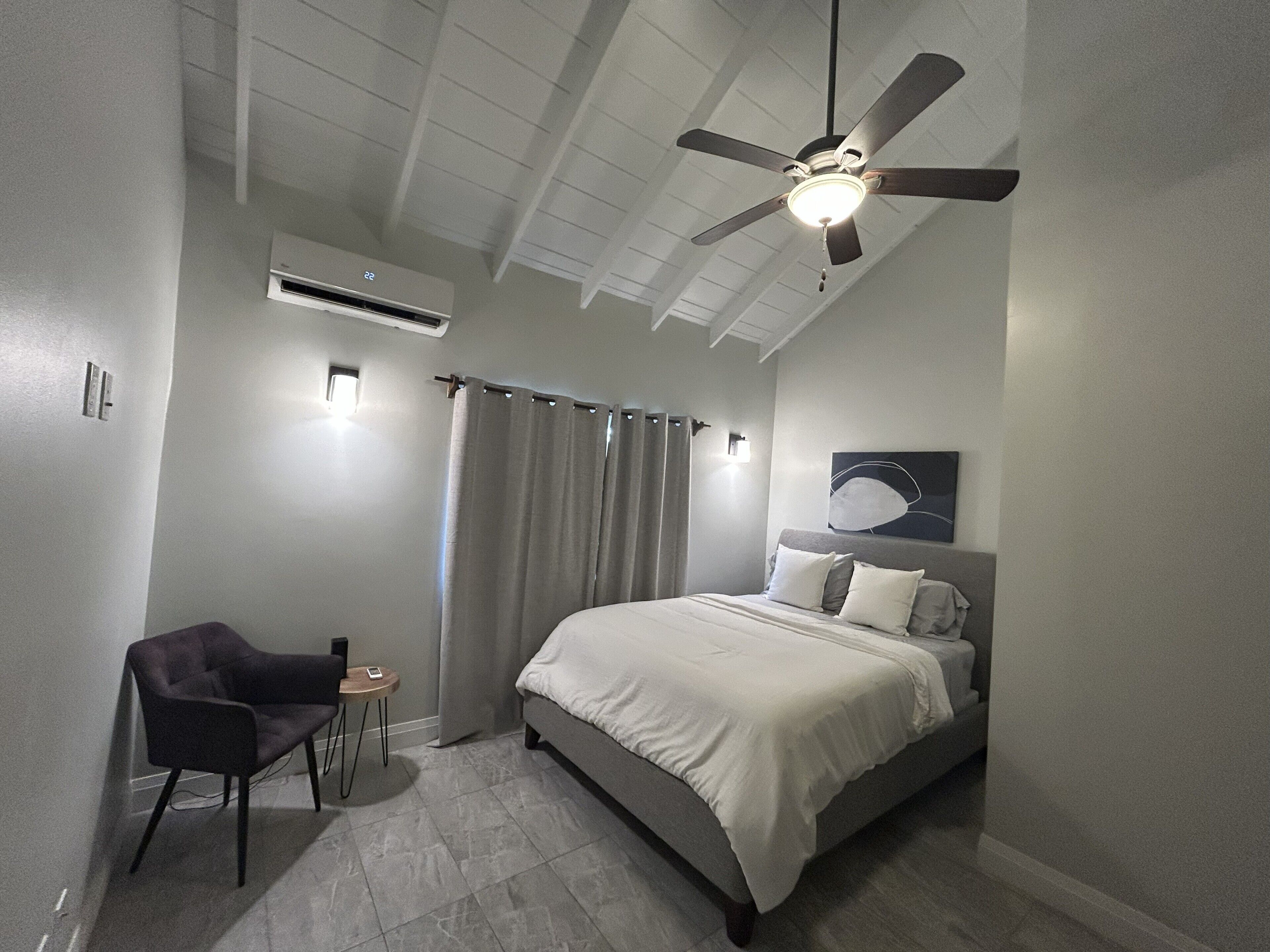 A bedroom with a bed, a chair, a ceiling fan, and an air conditioning unit.
