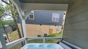 A hot tub on a wooden deck with a view of a house in the background. - Cabin with hot tub close to all the action! (Pigeon Forge)