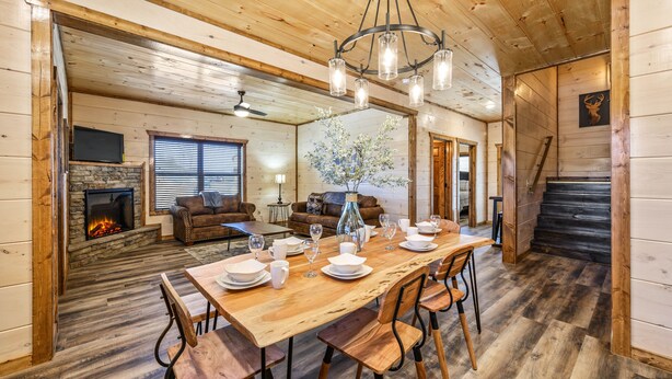 A wooden interior with a dining table set for six, a fireplace, a stone wall, and a staircase. - Cabin with hot tub close to all the action! (Pigeon Forge)