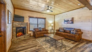 A cozy living room with a stone fireplace, two brown leather sofas, a wooden coffee table, and a ceiling fan. - Cabin with hot tub close to all the action! (Pigeon Forge)