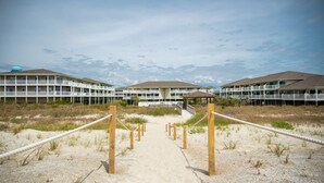 Een strandhotel met een zandpad dat leidt naar een overdekt gedeelte, omringd door strandbegroeiing.