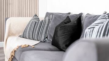 Ein graues Sofa mit gestreiften und einfarbigen Kissen, eine beige Tagesdecke und eine Wand aus Holzlatten im Hintergrund.