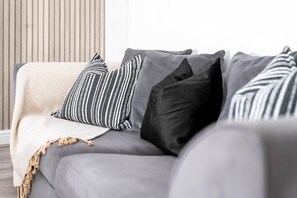 A grey sofa with striped and solid pillows, a beige throw blanket, and a wooden slat wall in the background.