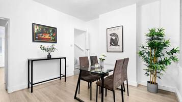 Ein moderner Essbereich mit einem Glastisch, einem schwarzen Metallgestell und braunen Polsterstühlen. Eine Topfpflanze und ein gerahmtes Kunstwerk sind an der Wand zu sehen.