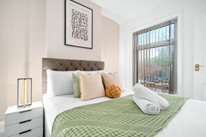 A neatly made bed with a green textured blanket, a headboard, and multiple pillows.