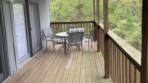 Een houten terras met een tafel en stoelen, met uitzicht op een bebost gebied.
