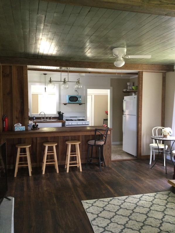A kitchen with wooden bar stools, a microwave, a stove, and a refrigerator.