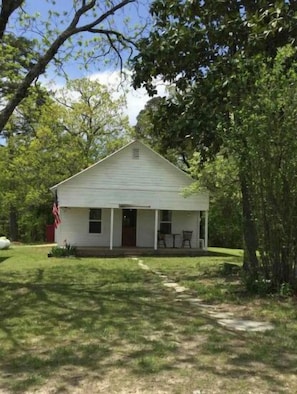 A small, single-story white building with a porch and two chairs outside.
