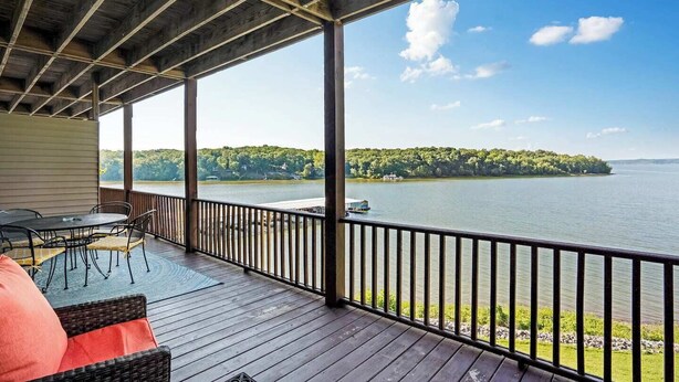A covered deck with a view of a lake and a forested island.