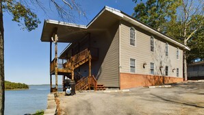 A two-story building with a wooden deck and a covered porch, situated by a body of water.