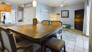 A spacious kitchen with a wooden dining table, chairs, and pendant lights. There is a refrigerator, a stove, and a ceiling fan.