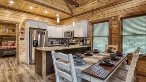 Una cocina de estilo rústico tipo cabaña, con vigas de madera, una isla central y un comedor con una mesa dispuesta para cuatro comensales.