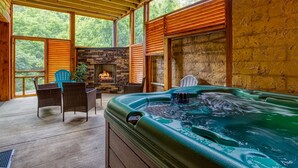Un jacuzzi con chimenea de piedra, terraza de madera y sillas de mimbre.