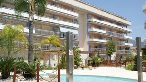 Un hotel a più piani con balconi, piscina e vegetazione tropicale.