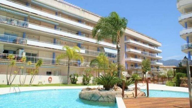 Un hotel con area piscina, numerosi balconi e palme.