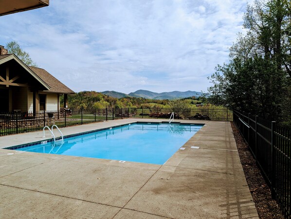 A rectangular swimming pool with a concrete deck, surrounded by a black metal fence, and a building with a sloped roof to the left. - Townsend Peaceful Side Smoky Mountains Near Cades Cove Hip Vintage Condo  (Townsend)