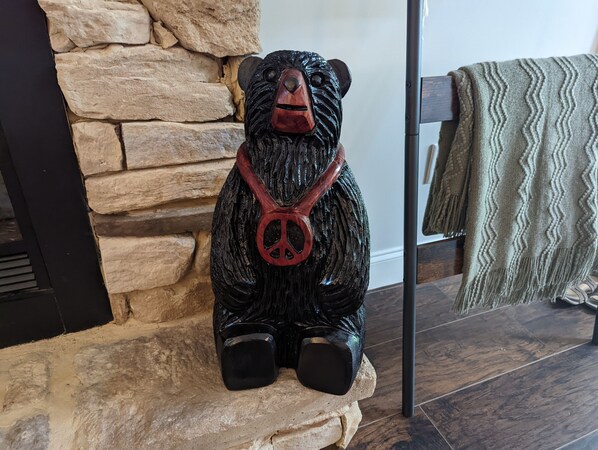 A wooden bear sculpture with a peace symbol pendant, placed on a stone ledge.