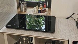A kitchen with a black induction cooktop, a window with a view of greenery, and a small shelf with kitchen utensils and condiments.