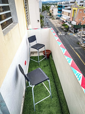 A balcony with two chairs, a potted plant, and a view of the street and buildings.