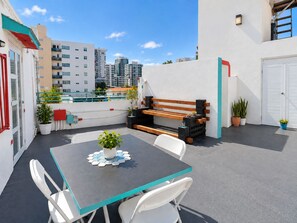 A rooftop terrace with a table, chairs, a bench, and potted plants.
