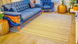 A living room with a blue sofa, a blue armchair, a patterned rug, and a large window with patterned curtains.
