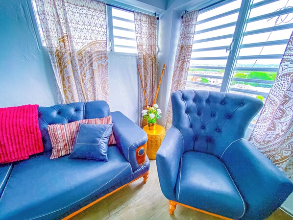 Una habitación con sofá y sillón azul, cortinas estampadas y vistas a zonas verdes.