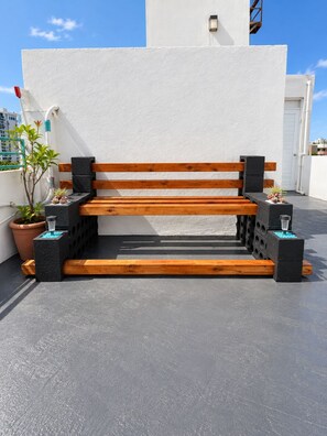 Un banco de madera con bloques negros en una terraza en la azotea.