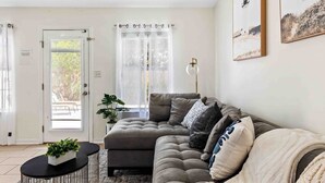 A modern living room with a sectional sofa, a small round table, and a potted plant. - Heated Pool • Steps to Beach w/ Private Access (Miramar Beach)