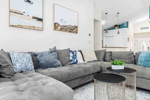 Uma sala de estar moderna com um sofá seccional cinza, uma mesa de centro redonda e duas luminárias pendentes fixadas na parede.