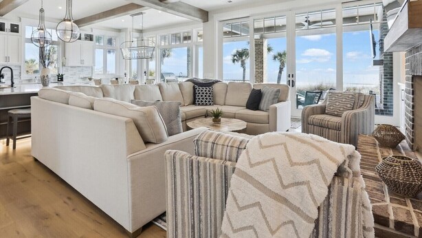Un vaste espace de vie comprenant un grand canapé, un fauteuil à rayures et une table basse. On y trouve également un ventilateur de plafond et une vue sur l’extérieur grâce à de grandes fenêtres.