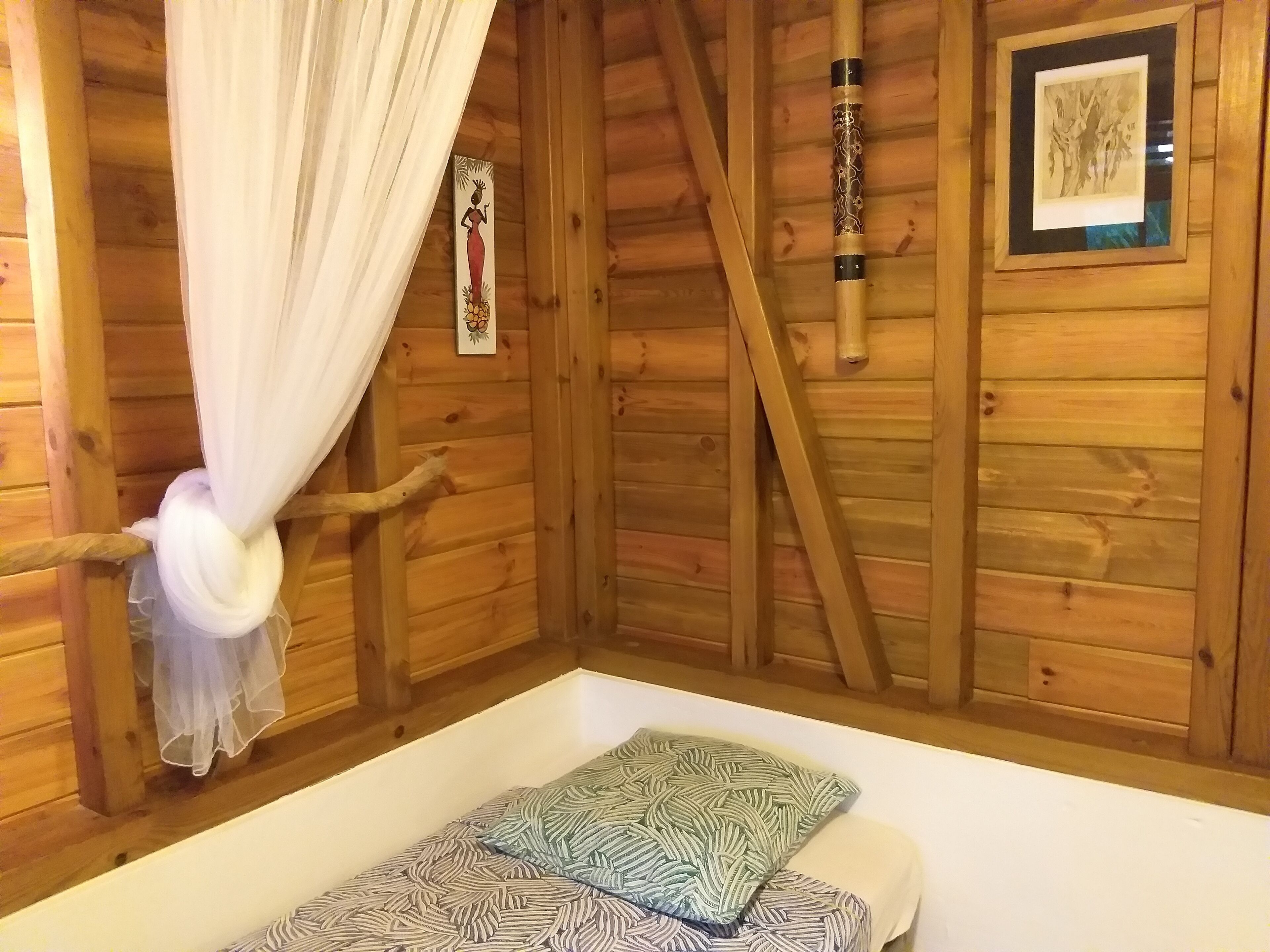 Une pièce de style cabane en bois, avec un lit, un rideau, un cadre photo et un objet décoratif accroché au mur.
