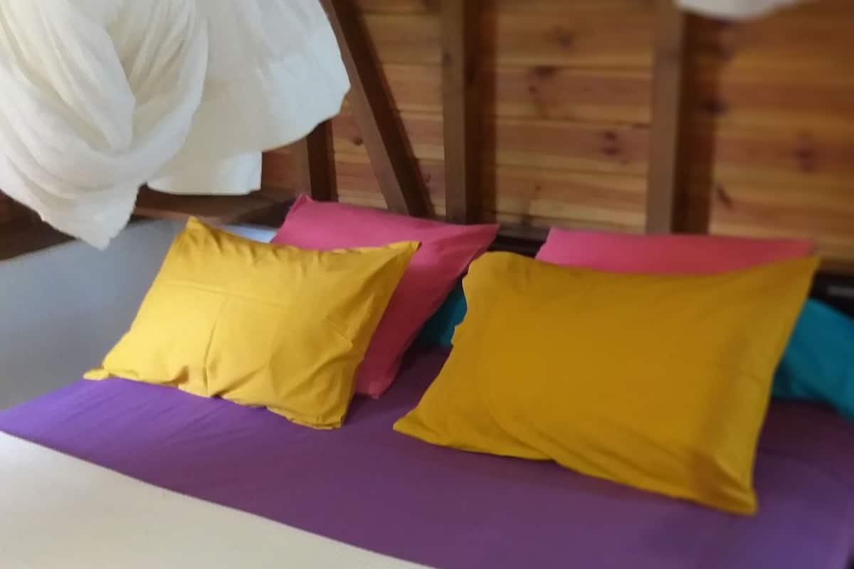 A bed with a purple mattress and two pillows, one yellow and one pink, in a room with wooden walls.