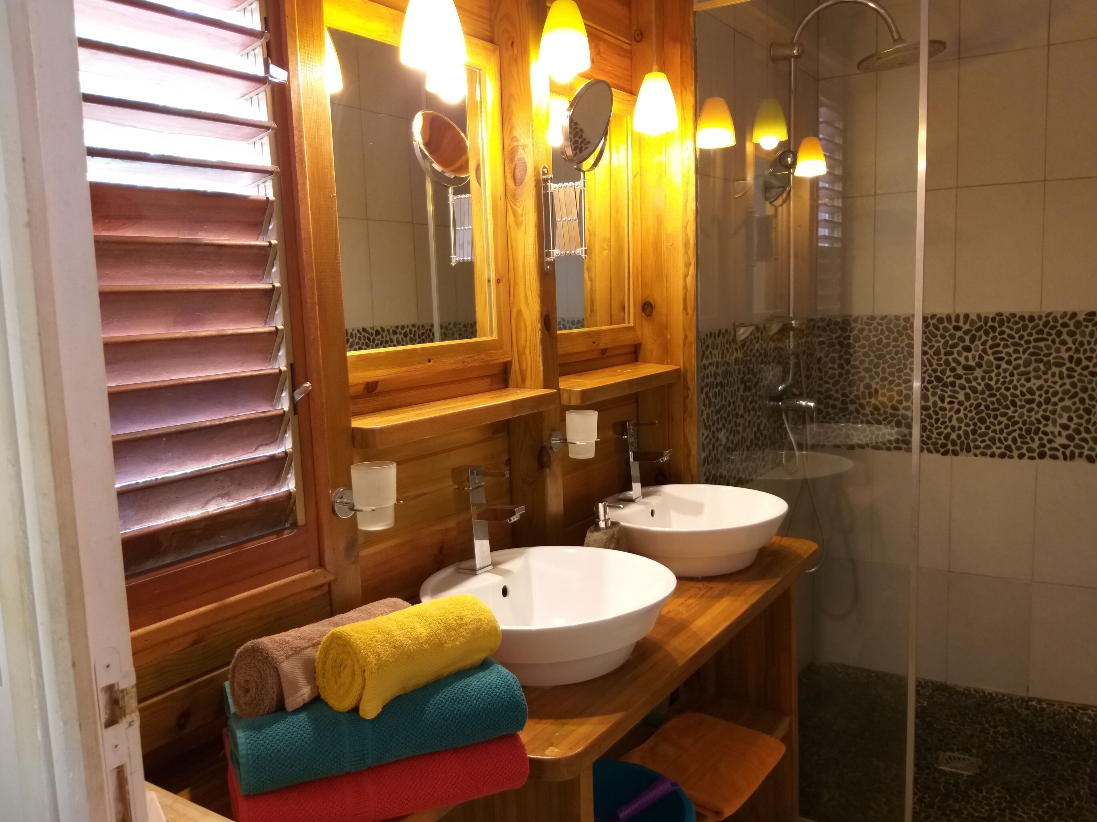 A wooden vanity with two sinks, a mirror, and a shower.