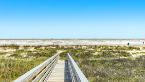 Ein hölzerner Steg führt zu einem Strand unter blauem Himmel.