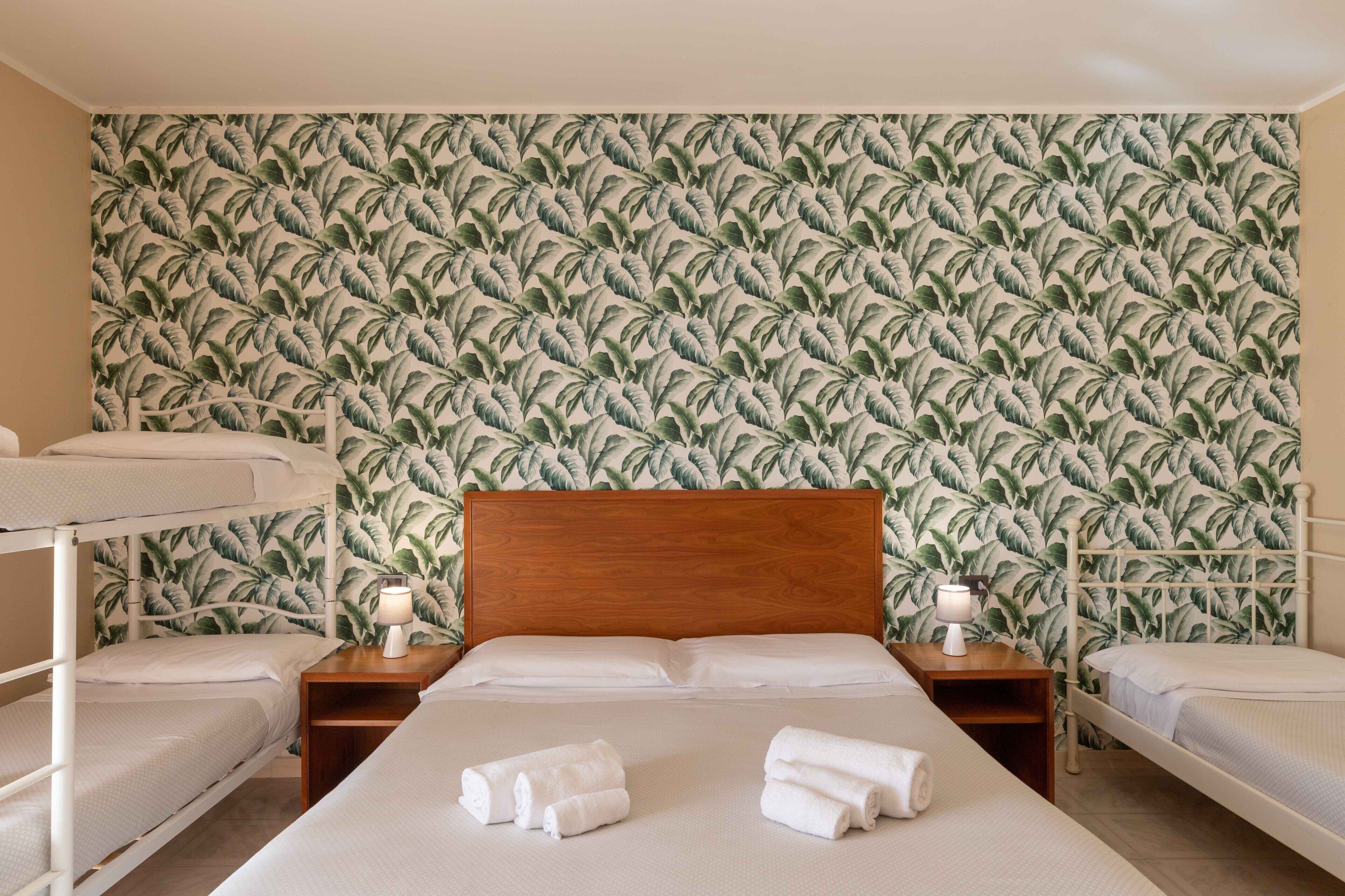 Habitación de hotel con literas, una cama individual y un papel tapiz con estampado de hojas tropicales.