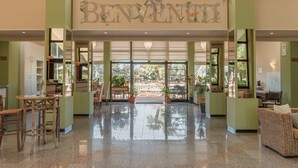 A spacious lobby with a 'BENVENUTI' sign, a chandelier, and potted plants. - Hotel Riva Etrusca (Bibbona)