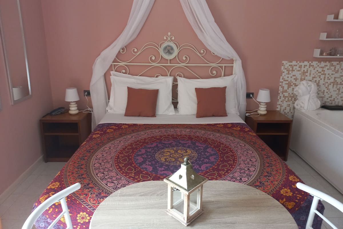 A bed with a canopy, two bedside tables with lamps, a patterned rug, and a small table with a lantern.