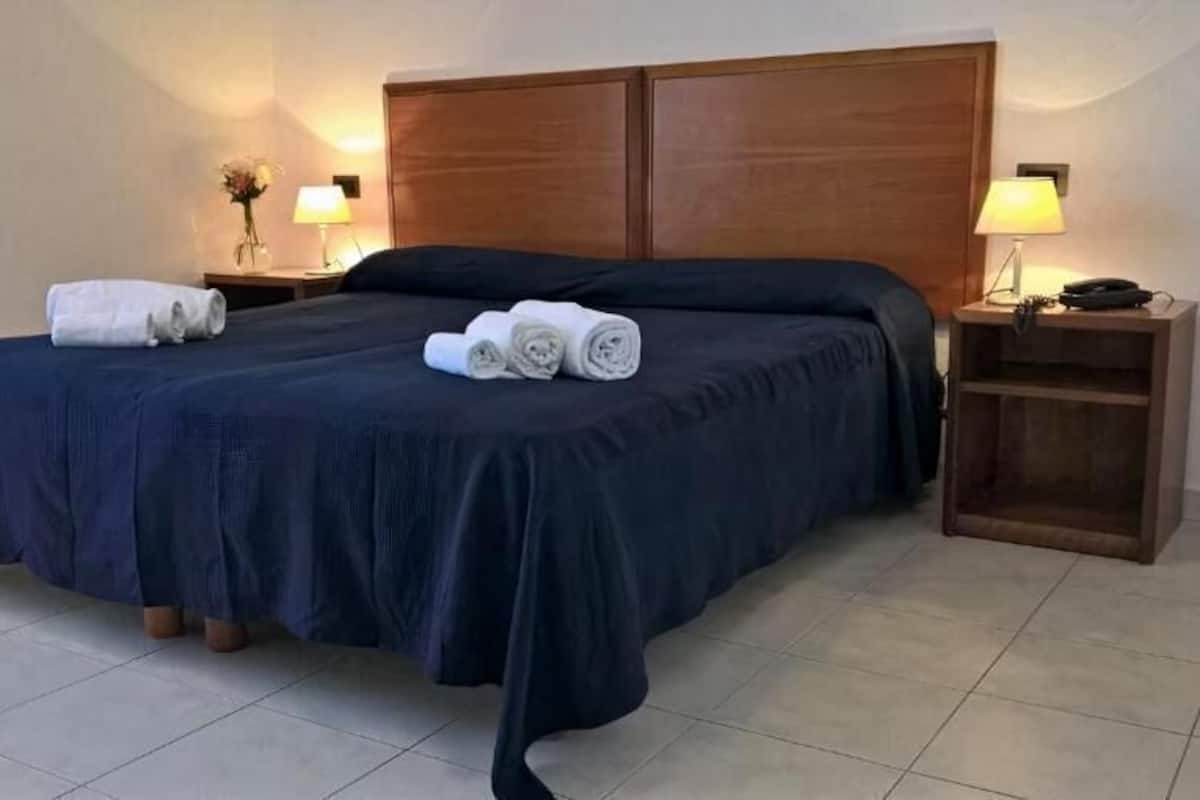 A hotel room with a bed, two bedside tables, and a nightstand.
