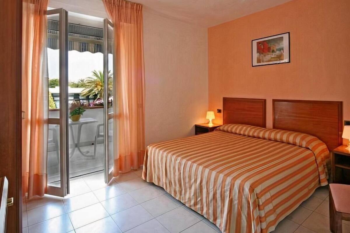A hotel room with a bed, a nightstand, a lamp, a picture on the wall, and a sliding glass door leading to an outdoor area.