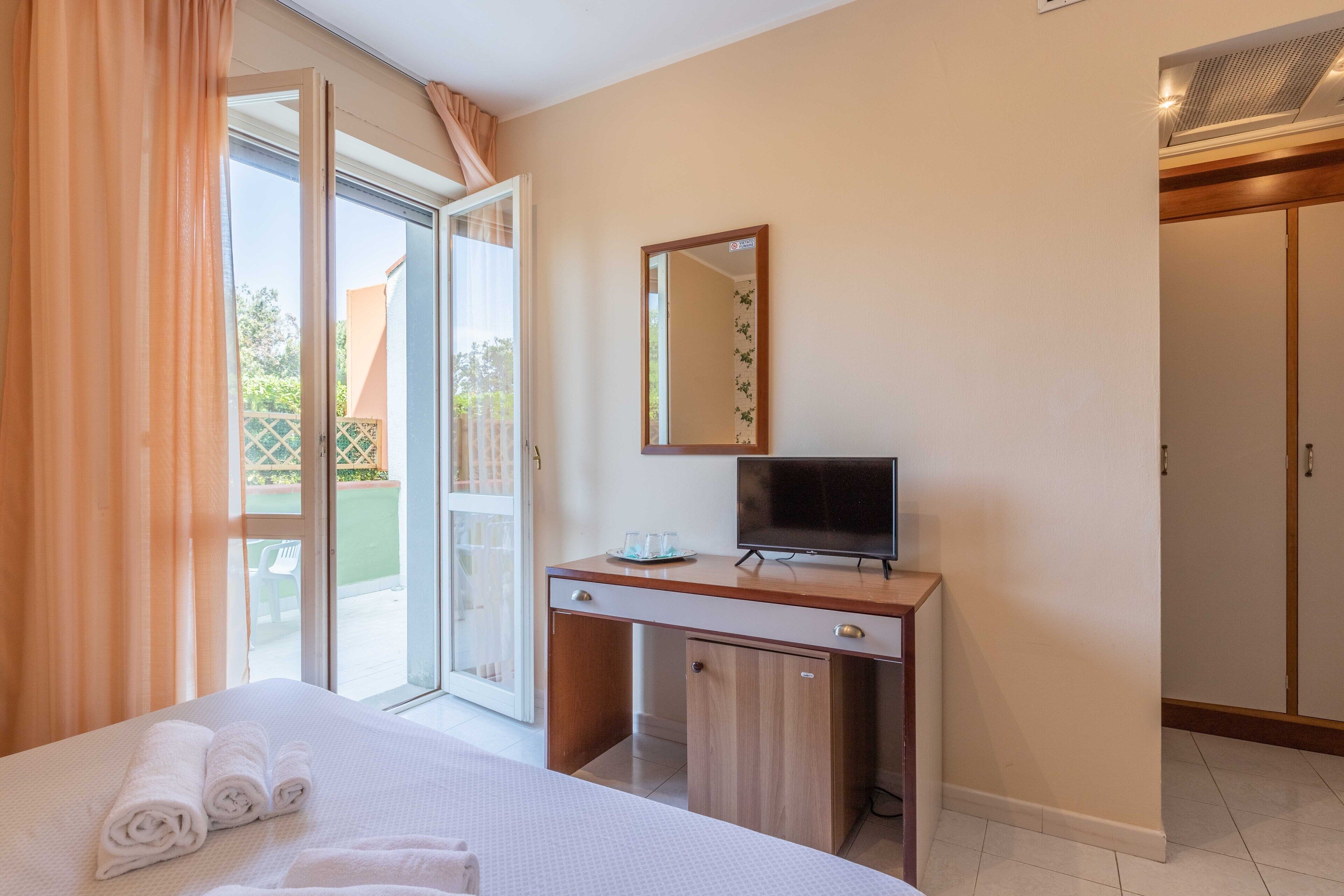 Habitación de hotel con cama, escritorio con televisor, puerta corrediza de vidrio al exterior y armario.