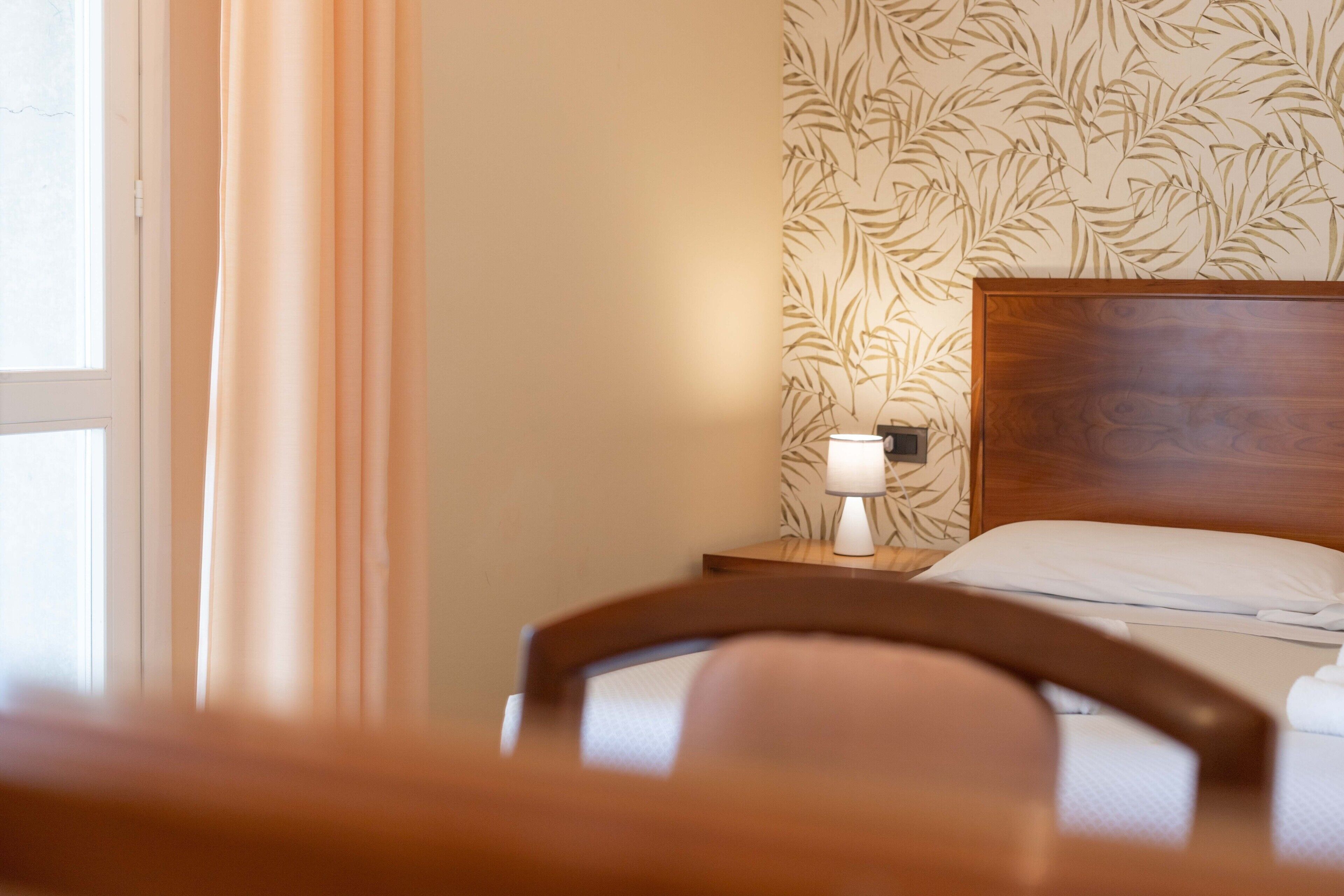Una habitación de hotel con una cama, una mesita de noche con lámpara y una ventana con cortinas.