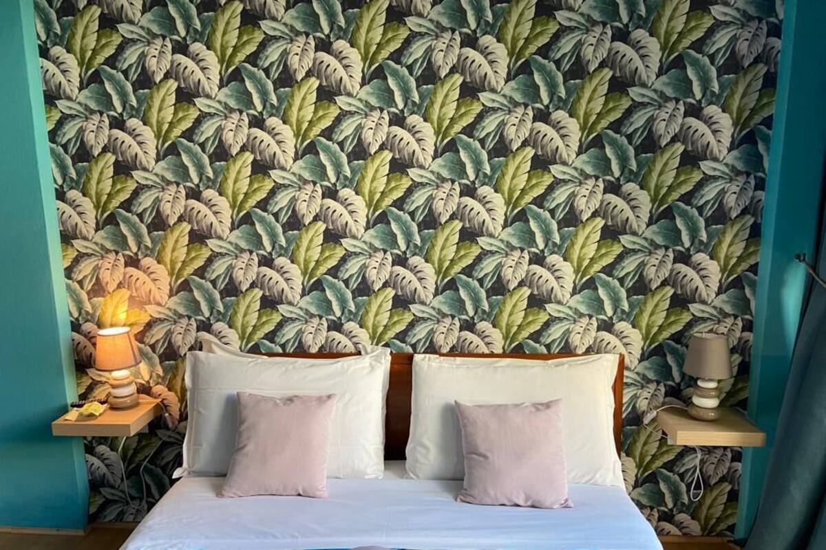 A bedroom with a bed, two bedside tables with lamps, and a wall with a leafy pattern.