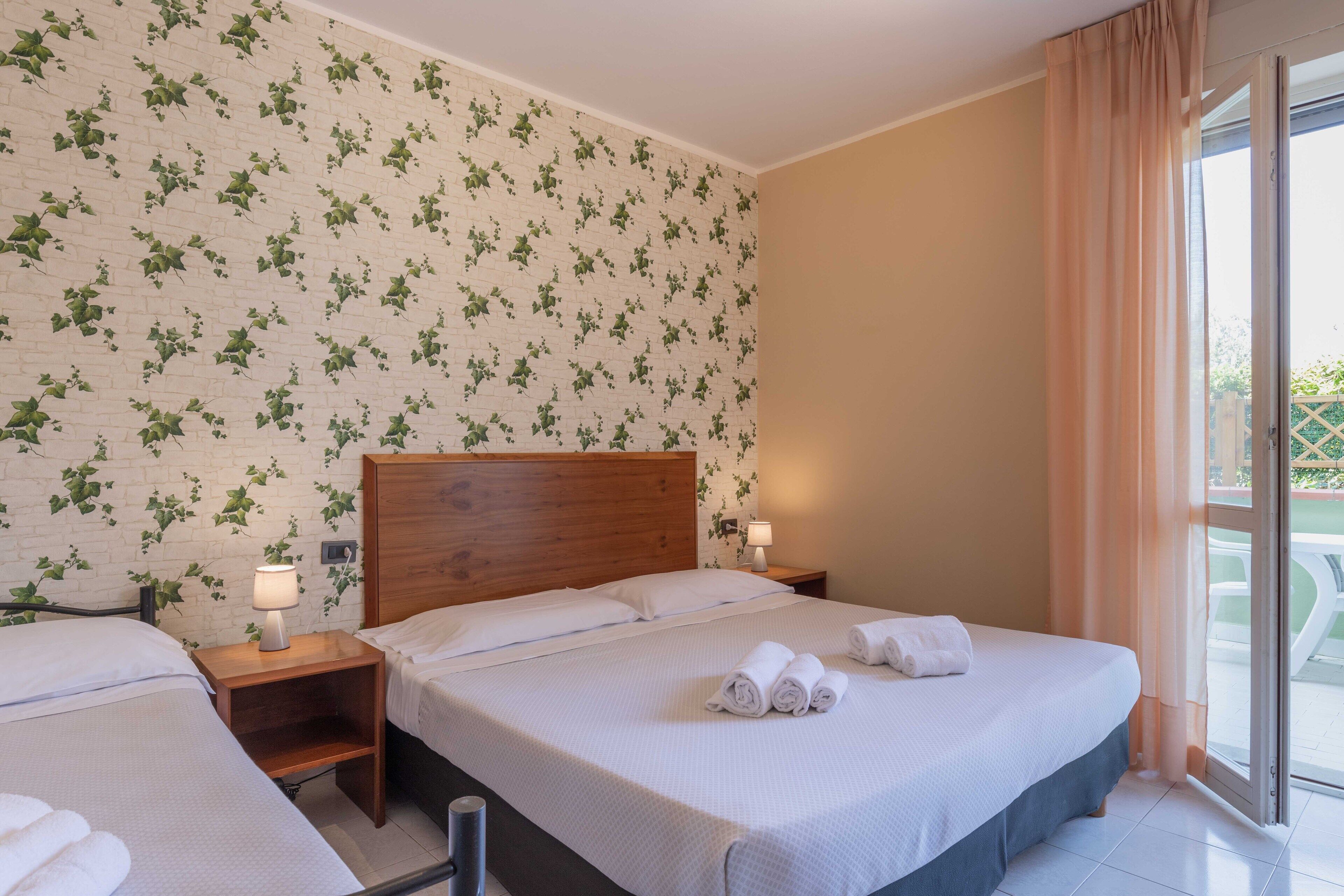 Ein Hotelzimmer mit Ziegelstein-Tapete, einem hölzernen Kopfteil, zwei Nachttischen mit Lampen und einem großen Bett mit zusammengerollten Handtüchern.