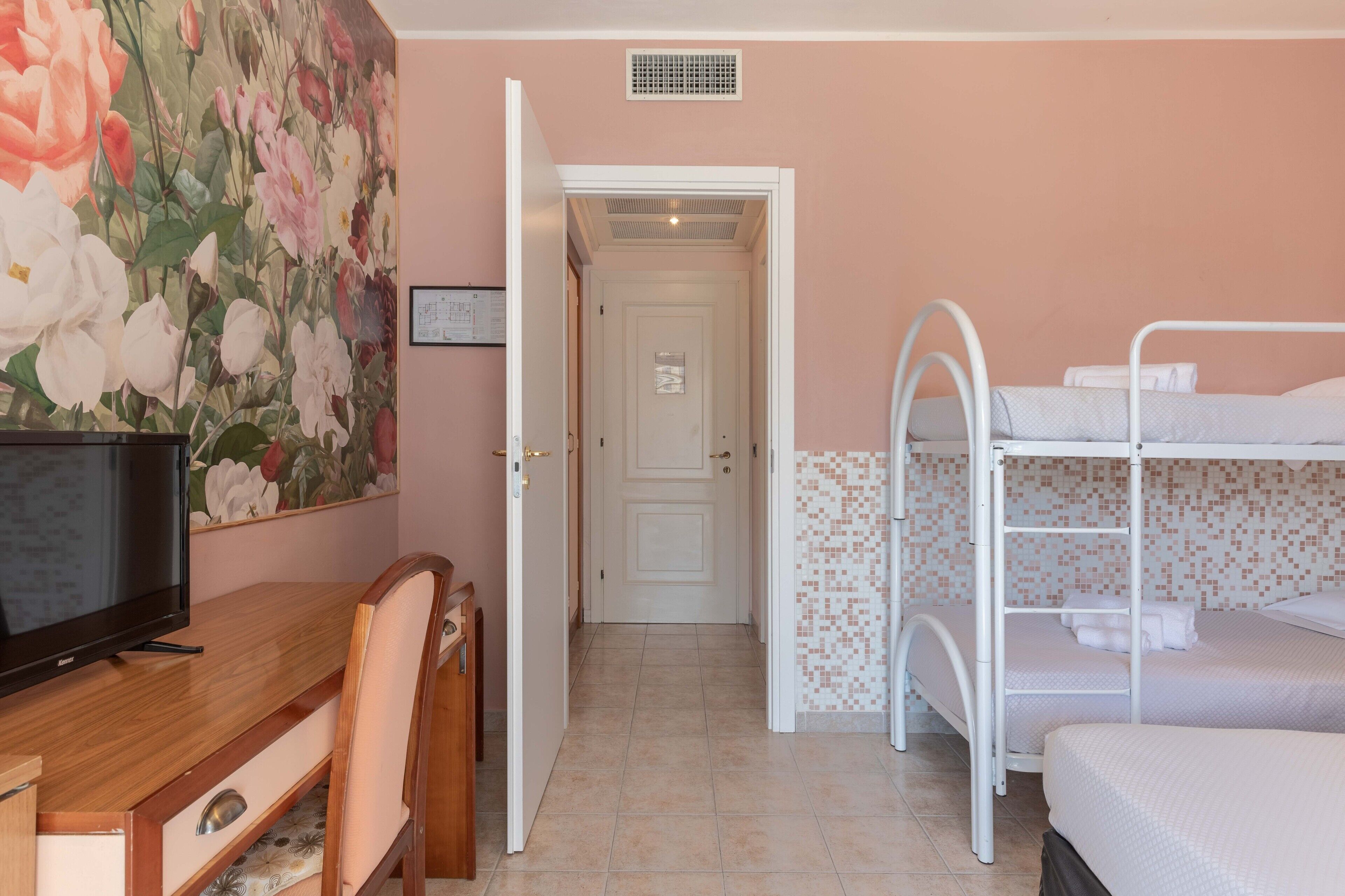 Una stanza con una scrivania in legno, una televisione, un letto a castello e una porta che dà su un'altra stanza.