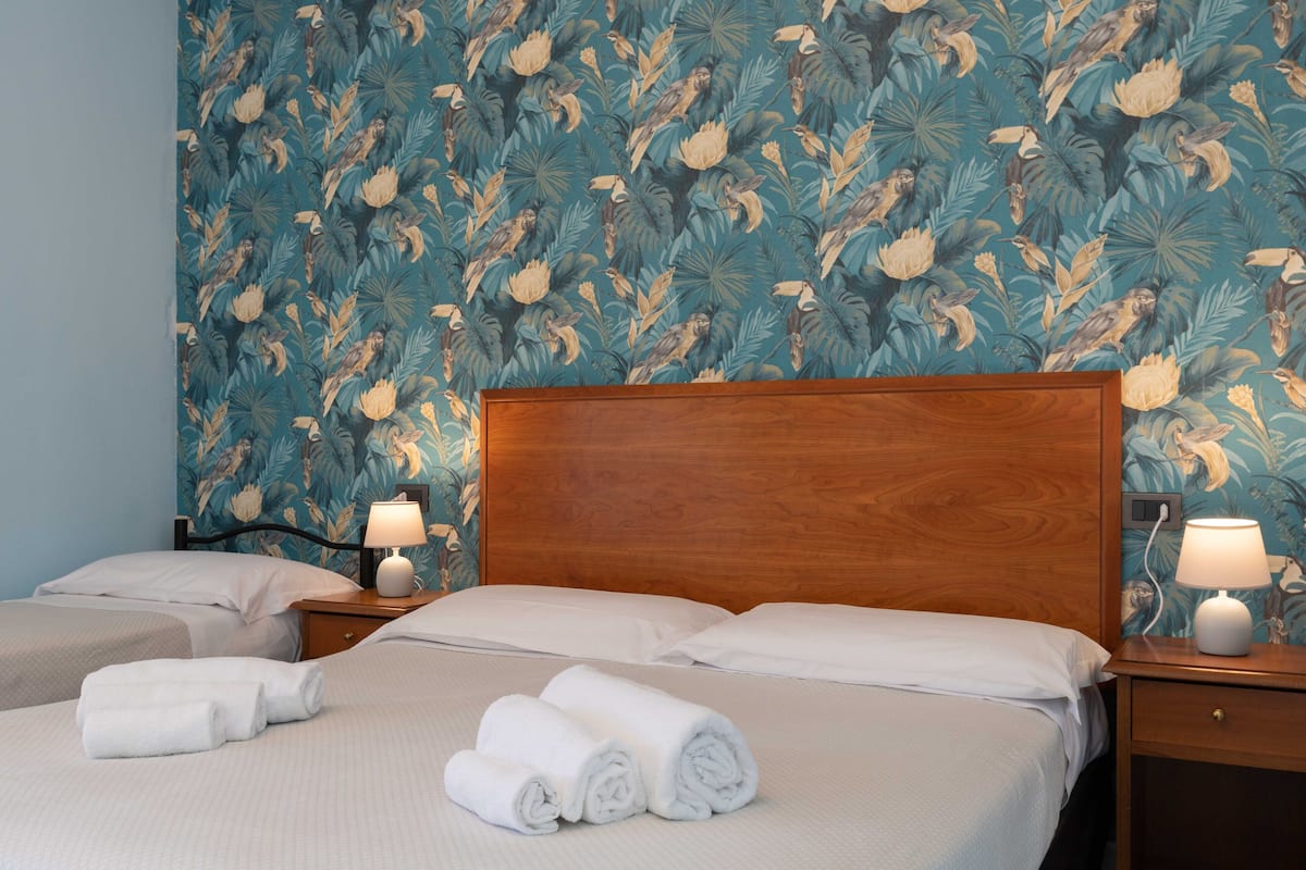 A hotel room with a bed, two bedside tables, and a wall with a tropical leaf pattern.