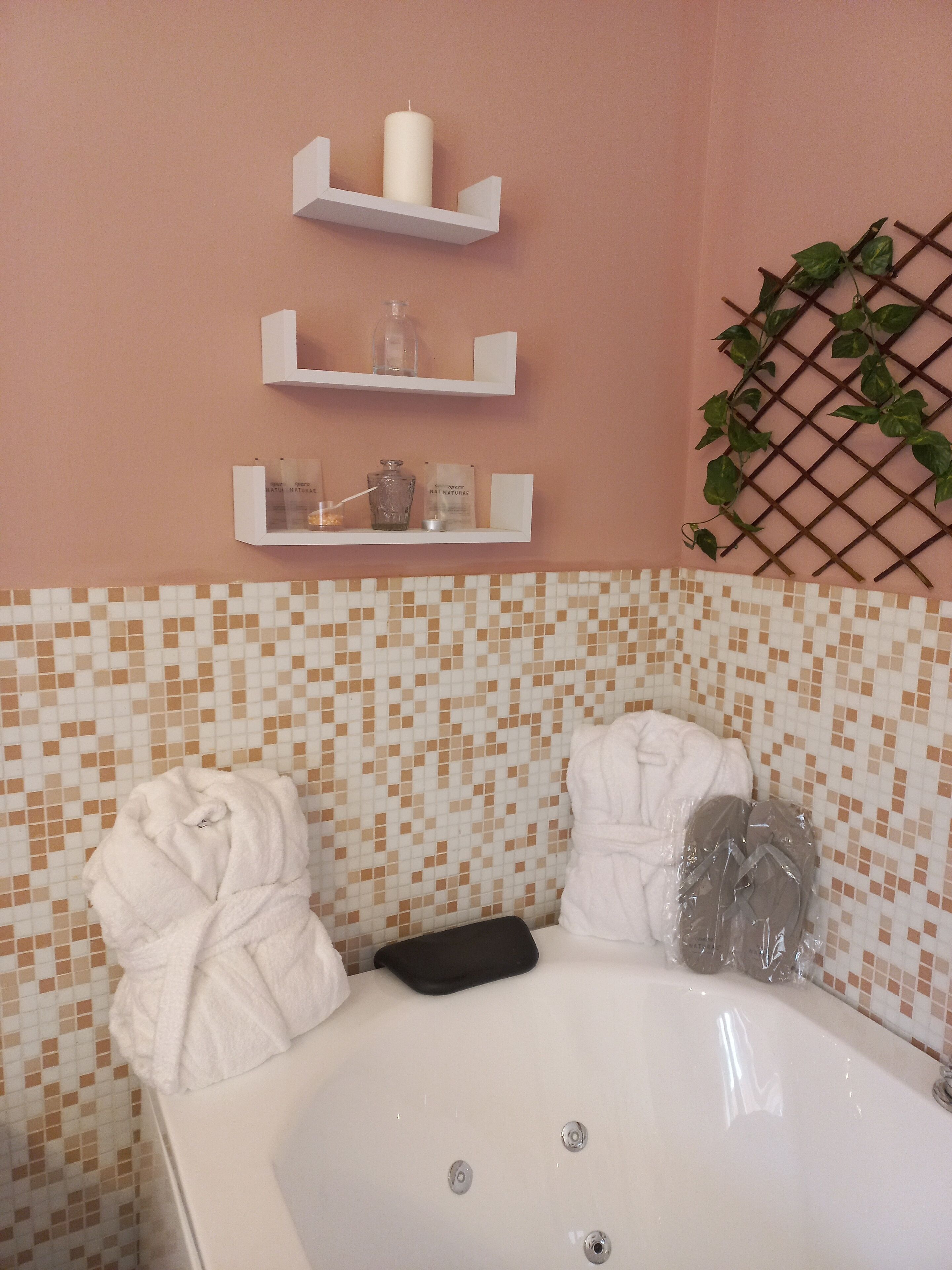 Un baño con una bañera, dos toallas blancas y tres estantes con diversos artículos de aseo.