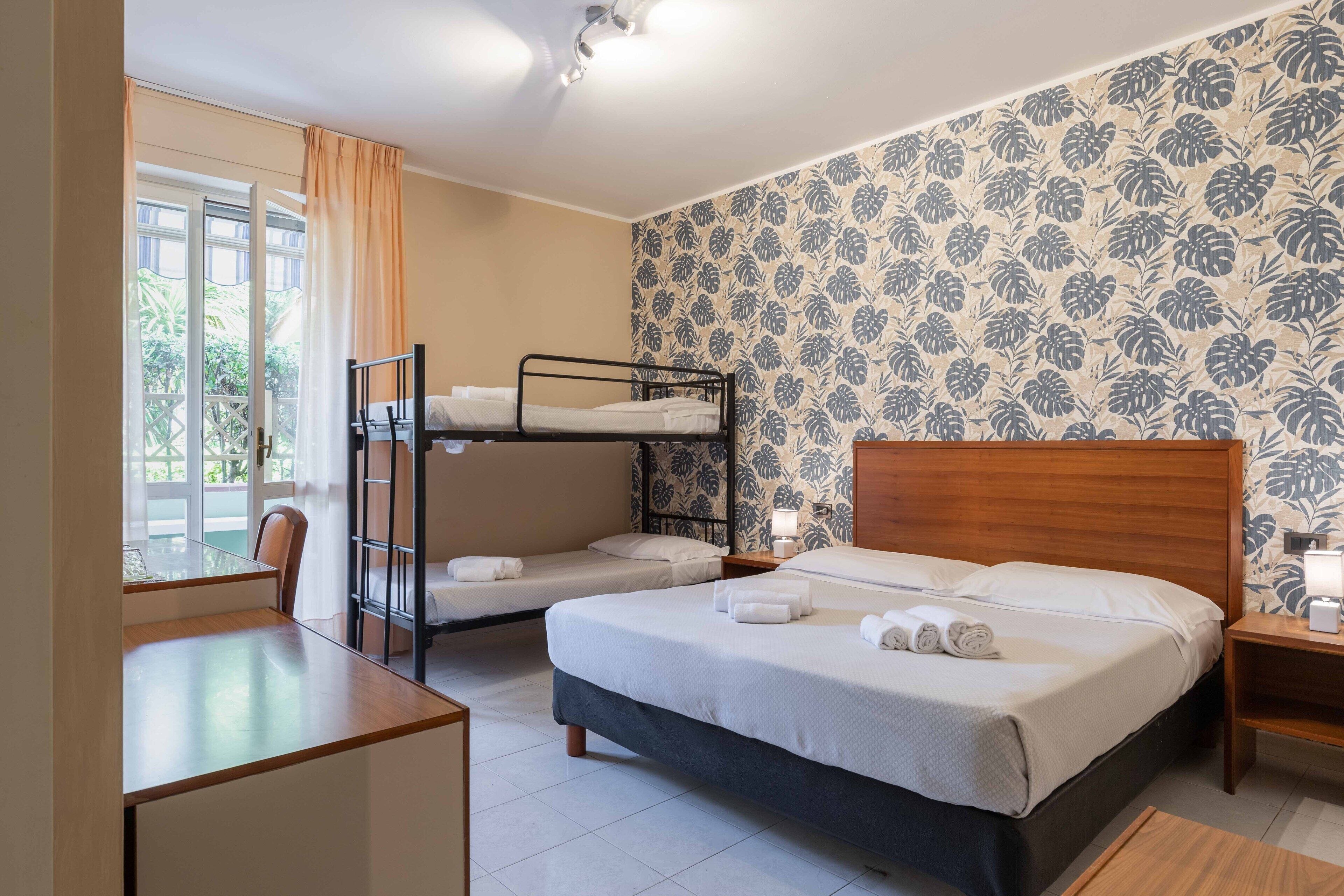 Ein Zimmer mit zwei Betten, einem Etagenbett, einem Holztisch und einem Fenster mit Vorhängen.