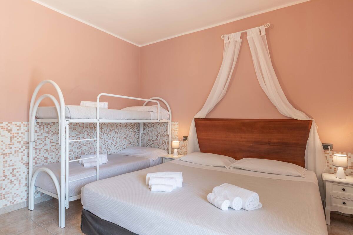 A hotel room with bunk beds, a canopy bed, and a nightstand with a lamp.