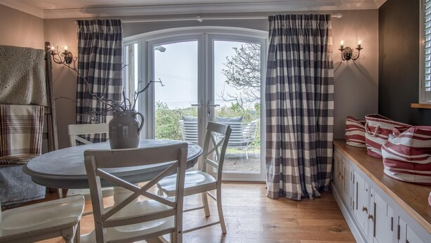 A dining area with a round table, white chairs, a vase, and a view through a glass door to the outside. - Highfield - 3 Bedroom Holiday Home - Llanmadoc (Swansea)